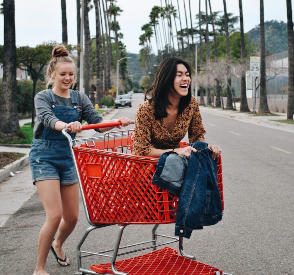 woman riding shopping cart with another woman pushing it in the middle of road
